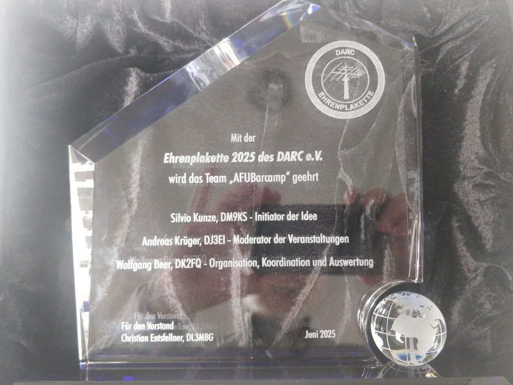 Foto der Ehrenplakette des DARC. Zu sehen ist eine dicke, unregelmäßige Glasscheibe
 mit gravierter Beschriftung.